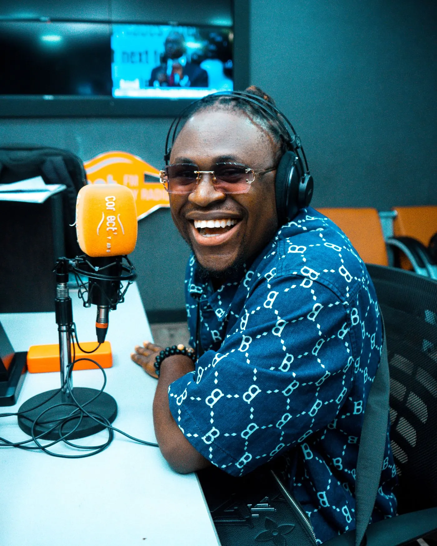 A smiling presenter wearing headphones sits at a studio microphone.